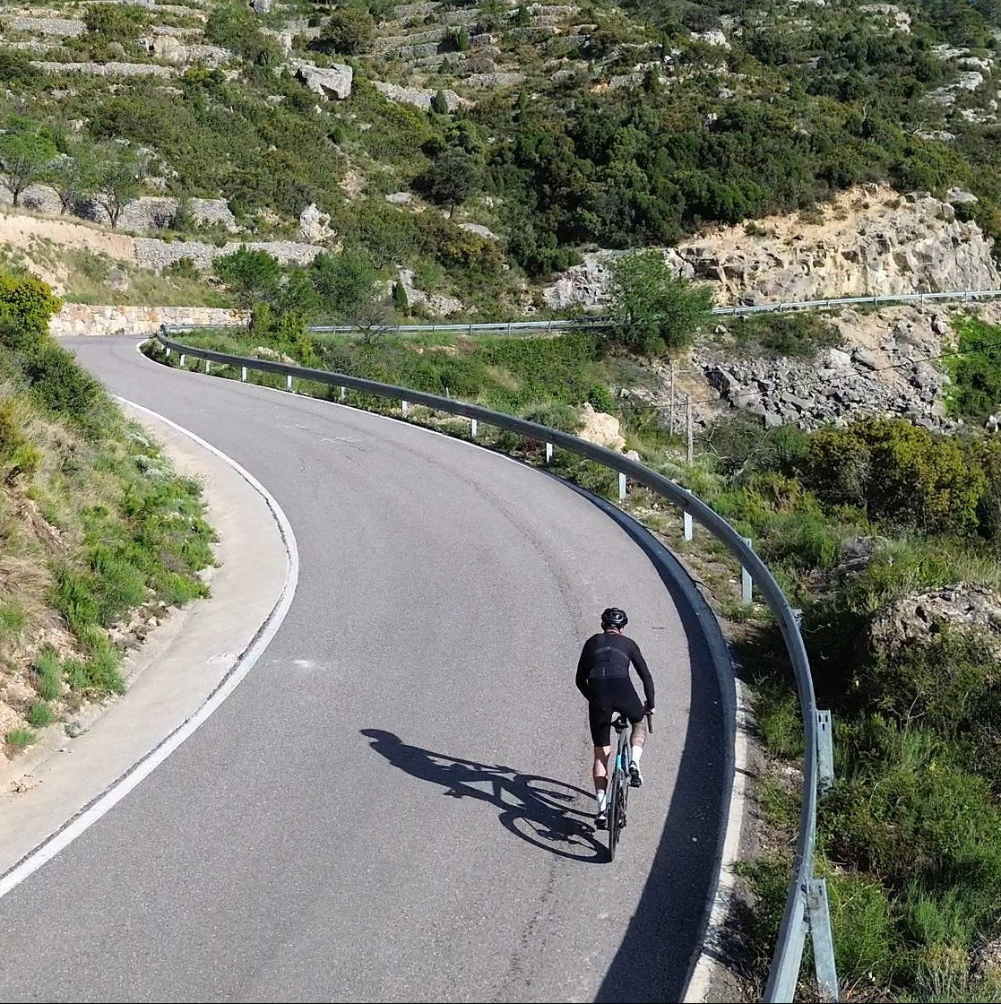 Person cycling on a winding road surrounded by greenery